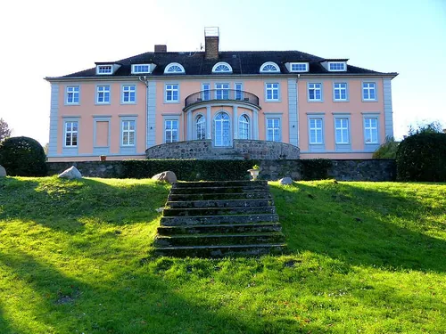 Gartenseite des Herrenhauses Lübbenow mit apricotfarbener Fassade, halbrunder Seeterrasse und Freitreppe